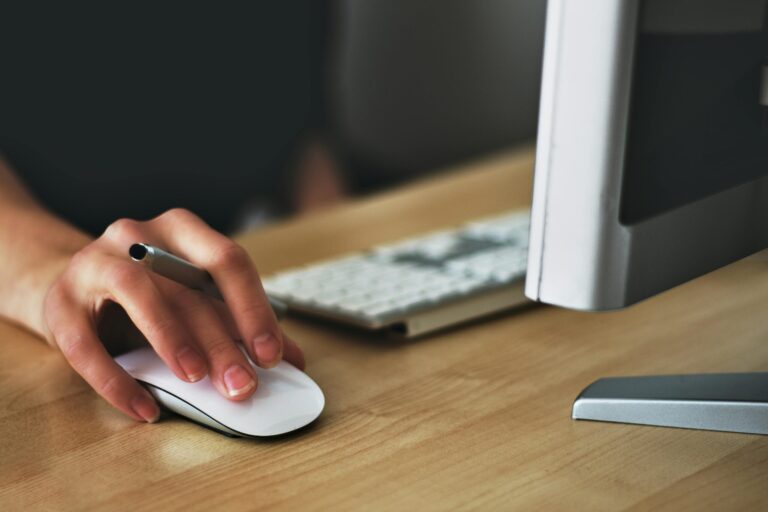 Free A hand using a wireless mouse at a modern desk setup with a computer and keyboard. Stock Photo